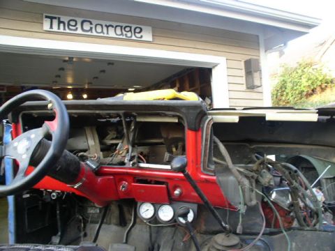 1979 Ford Bronco - Vehicle interior with dashboard removed, showing wiring and gauges. Sign reads 'The Garage'.