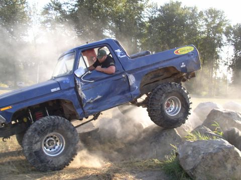 1979 Ford Bronco - A heavily modified blue pickup truck is shown off-roading over large rocks.