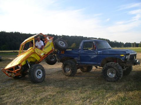1979 Ford Bronco - A blue pickup truck is lifting a yellow off-road buggy in a grassy field under a partly cloudy sky.
