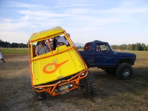 1979 Ford Bronco - A yellow buggy with an orange roll cage is parked next to a blue pickup truck in an open field.