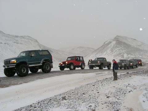 2001 Jeep Wrangler - A group of off-road vehicles travels in a convoy through a snowy mountain landscape.