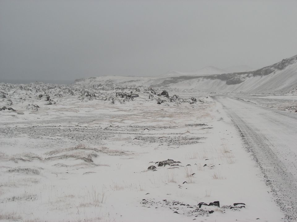 Snowy landscape with a dirt road winding through rocky terrain under an overcast sky