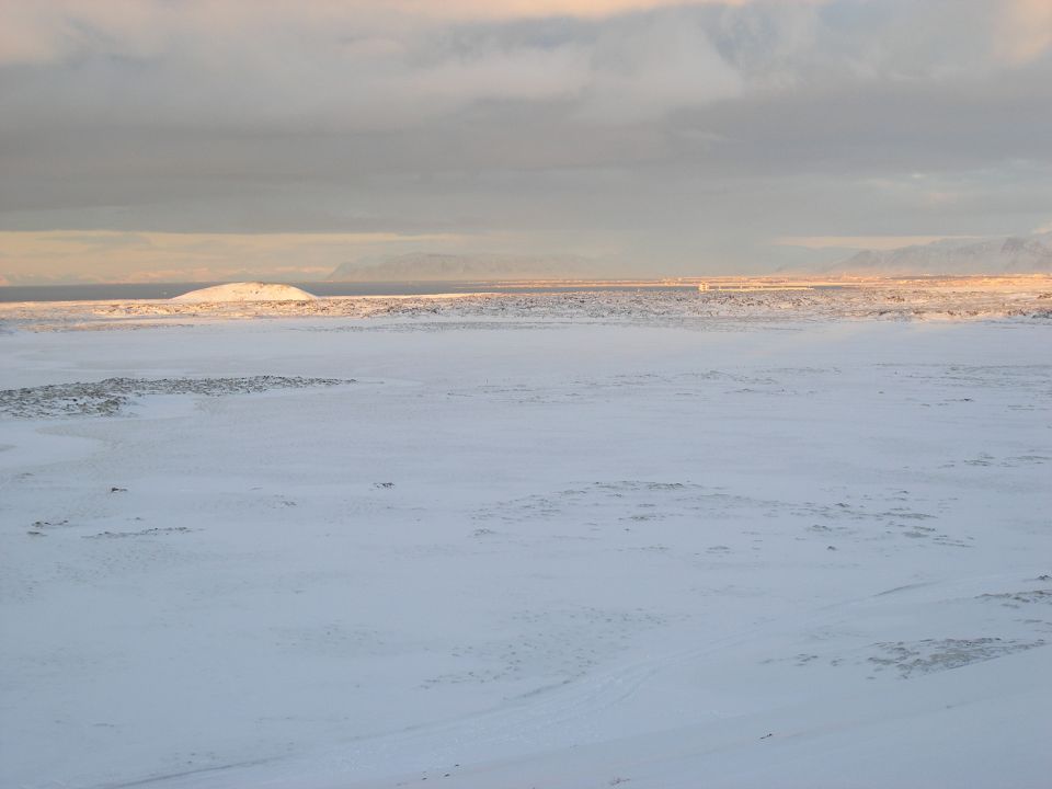 Vast snowy plain under a cloudy sky, with a small hill in the distance. Watermark reads SUPERMOTORS