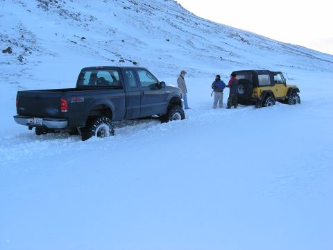 2001 Jeep Wrangler - Two off-road vehicles are partially submerged in snow on a hillside, with several individuals observing the scene.