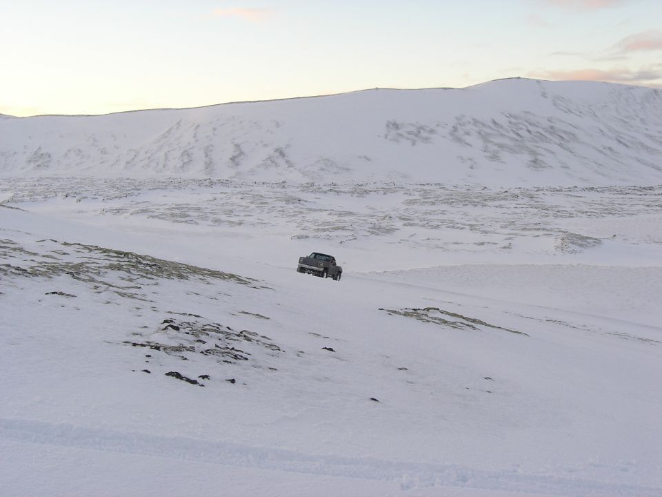 Dark pickup truck driving on a snowy, desolate landscape with mountains in the background