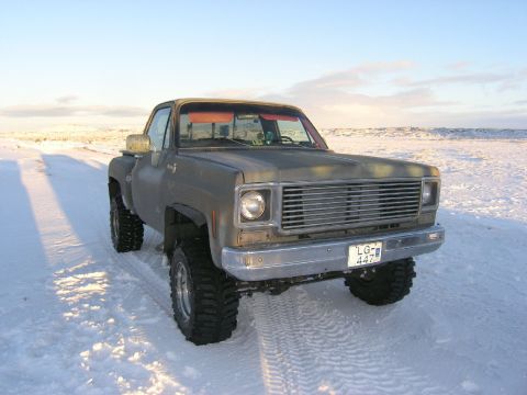 2001 Jeep Wrangler - This lifted pickup truck is equipped with large off-road tires and is parked in a snowy landscape.