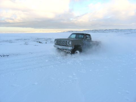 2001 Jeep Wrangler - A pickup truck navigates a snowy landscape, its tires kicking up a cloud of snow.