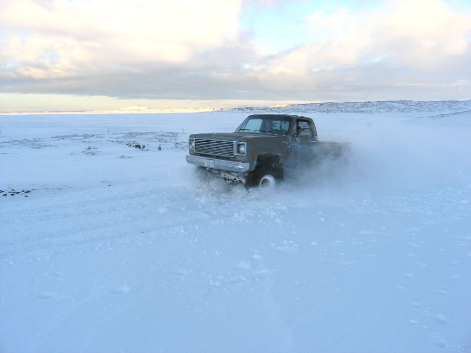 Pickup truck drifting in a snowy field, kicking up snow