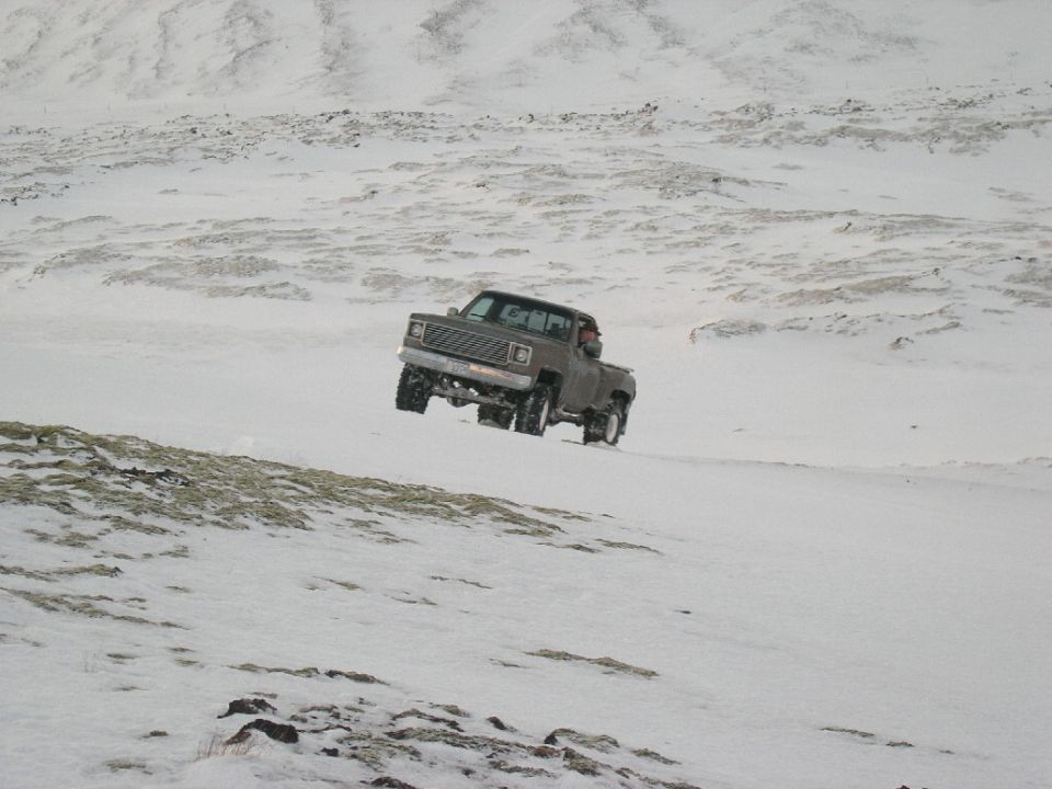 Brown pickup truck with lifted suspension driving on a snow-covered hill