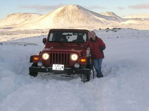 2001 Jeep Wrangler - A red 2001 Jeep TJ is partially submerged in snow, with a woman posing beside it against a backdrop of snowy mountains.