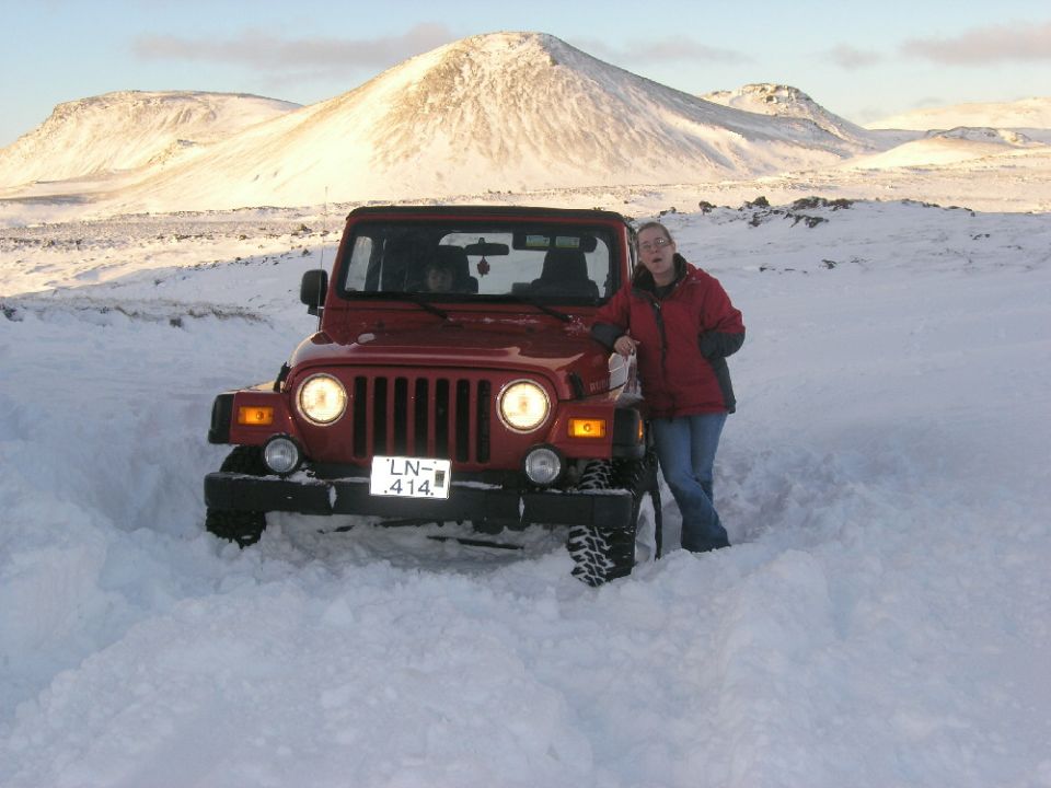 Red 2001 Jeep TJ in snow, front view, with a woman standing next to it