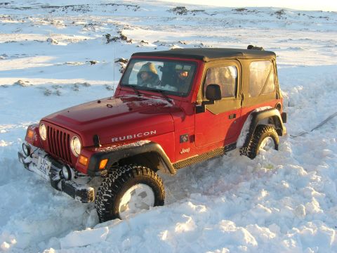 2001 Jeep Wrangler - A red Jeep Wrangler Rubicon navigates a snowy landscape, with two occupants visible inside.