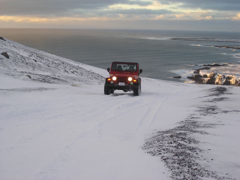 2001 Jeep Wrangler - A red Jeep Wrangler navigates a snow-covered coastal landscape under a cloudy sky.