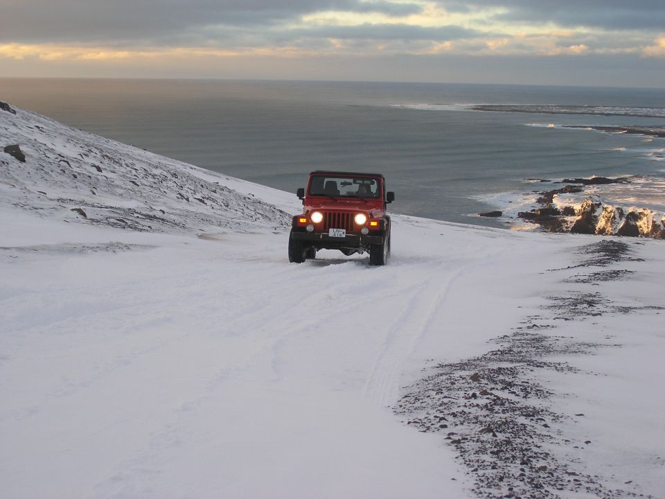Red Jeep Wrangler driving on a snowy hill overlooking the ocean