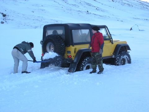 2001 Jeep Wrangler - Two people dig a yellow 2001 Jeep TJ out of deep snow in a remote, snowy landscape.