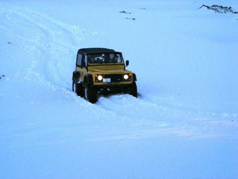 2001 Jeep Wrangler - A yellow Land Rover Defender navigates a snowy terrain, leaving tracks behind.