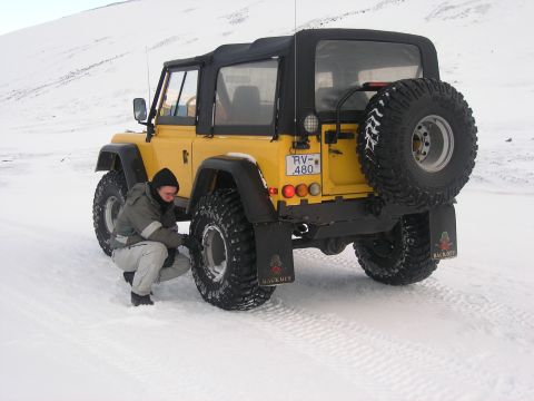 2001 Jeep Wrangler - A yellow off-road vehicle with a soft top is parked in a snowy landscape while a person checks one of its tires.