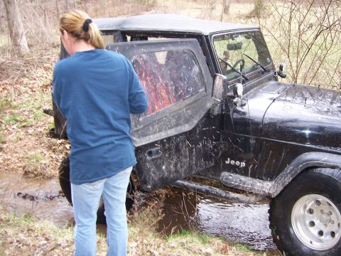 1999 Jeep TJ - A black Jeep Wrangler is stuck in a muddy ditch with its driver's door open.