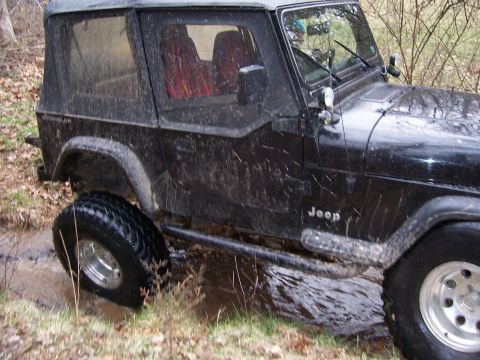 1999 Jeep TJ - This 1999 Jeep TJ navigates a muddy trail, its tires kicking up water.