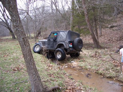 1999 Jeep TJ - Jeep TJ off-roading through a shallow, muddy creek in a forest setting.