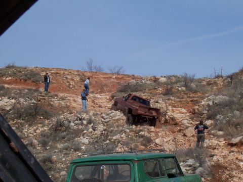 2004 Aston Martin Virage - A red pickup truck navigates a challenging rocky path, with several onlookers observing the off-road adventure.