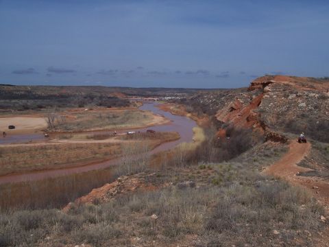 2004 Aston Martin Virage - Off-road vehicles navigate a river and trails in a , arid landscape under a blue sky.