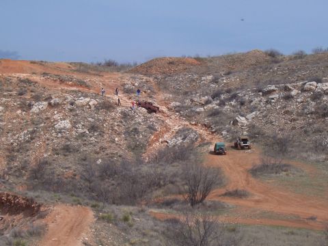 2004 Aston Martin Virage - Several off-road vehicles traverse a challenging dirt track in a , arid landscape, with onlookers present.