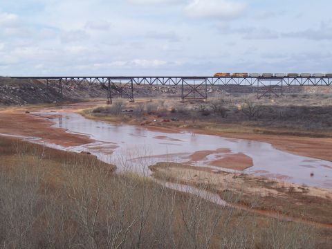 2004 Aston Martin Virage - A train travels across a high bridge spanning a river with a muddy, red-colored bed.