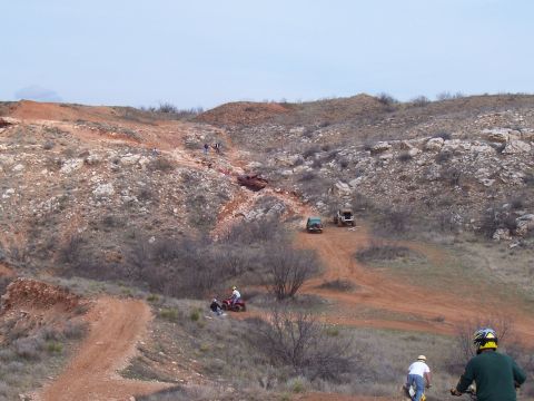 2004 Aston Martin Virage - Off-road vehicles navigate a challenging dirt track in a , hilly terrain under an overcast sky.