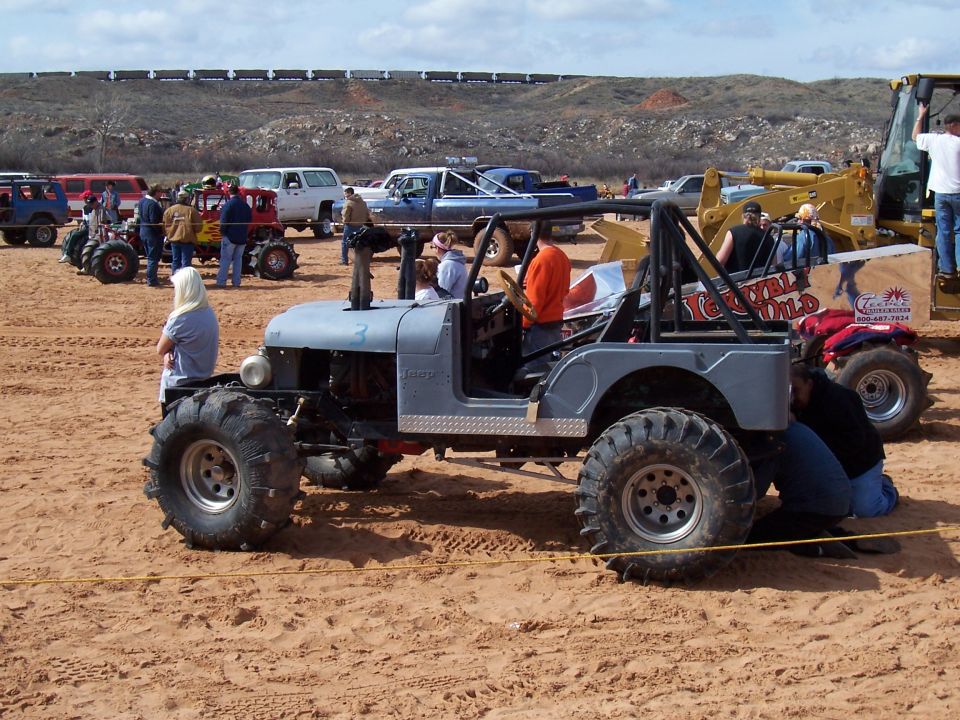 Gray modified jeep with large tires and roll cage on sandy terrain