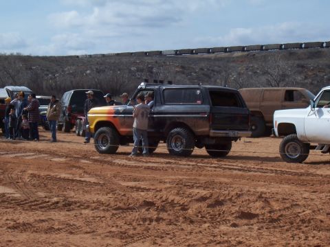 2004 Aston Martin Virage - Several people gather around a lifted, off-road SUV in a muddy, outdoor setting, with a train visible in the background.