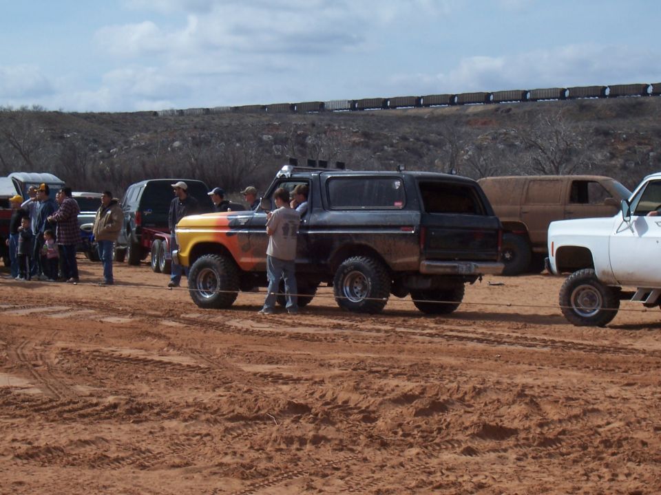 Lifted black and orange SUV in a muddy field with people nearby