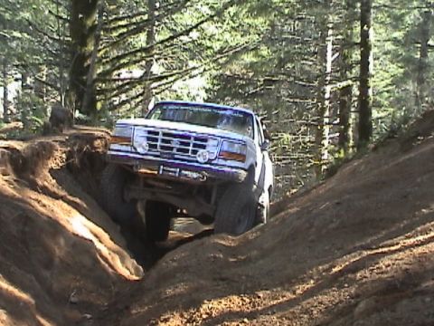 1994 Ford Explorer - A white Ford Bronco II navigates a challenging off-road trail, climbing a steep dirt incline.