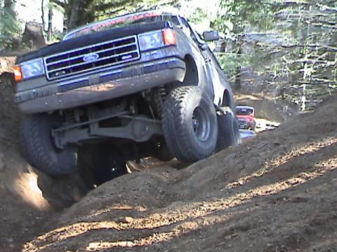 1994 Ford Explorer - A black Ford Bronco II navigates a steep dirt incline, with another red vehicle visible in the background.