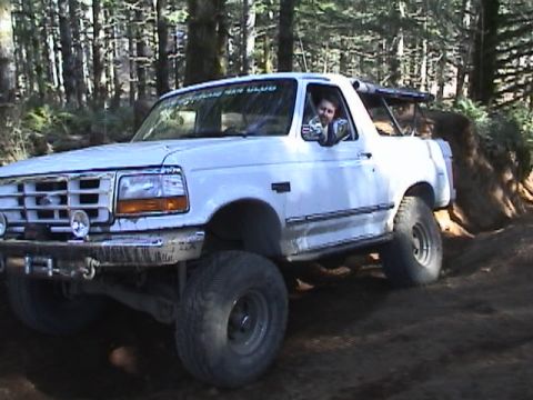 1994 Ford Explorer - A white Ford Bronco navigates a wooded trail, with a driver visible through the window and a club decal on the windshield.
