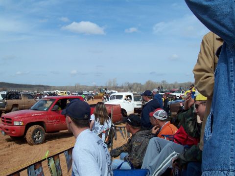 2004 Aston Martin Virage - A red pickup truck navigates a muddy track during an event, with spectators watching from the side.