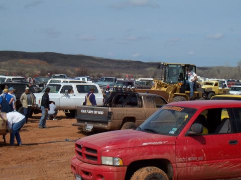 2004 Aston Martin Virage - A muddy scene with several trucks and a large yellow loader at an outdoor event.