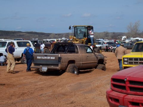 2004 Aston Martin Virage - A muddy pickup truck is stuck in the sand at an off-road event, with a bulldozer nearby and other vehicles in the background.