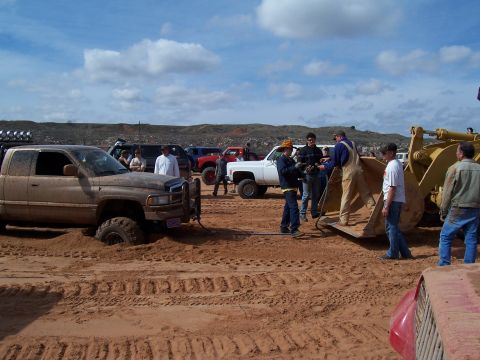 2004 Aston Martin Virage - Several vehicles and people are gathered in a sandy area, with one truck deeply stuck in the mud.