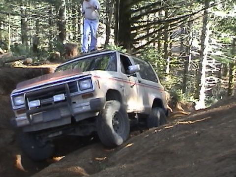 1994 Ford Explorer - A Ford Bronco II navigates a challenging off-road trail in a wooded area.