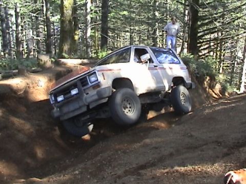 1994 Ford Explorer - An off-road vehicle navigates a challenging dirt track in a wooded area, with a person observing from the roof.