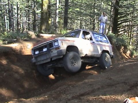 1994 Ford Explorer - A white Ford Bronco II navigates a steep dirt incline on a wooded trail.
