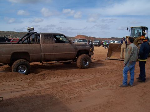 2004 Aston Martin Virage - Muddy pickup truck stuck in sand, assisted by a bulldozer at an outdoor event.