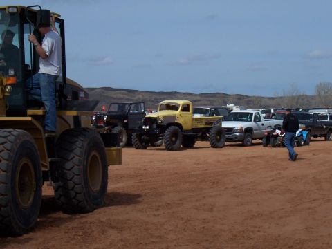 2004 Aston Martin Virage - A collection of modified trucks and vehicles are gathered on a dirt lot under a clear sky.