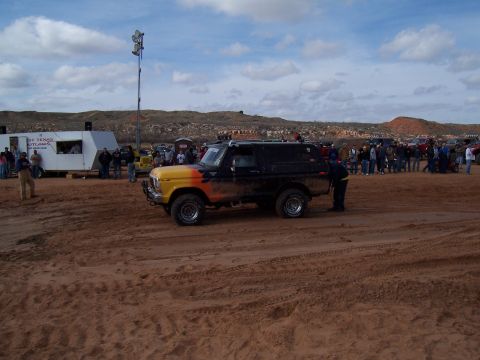 2004 Aston Martin Virage - A modified Ford Bronco with custom paint sits on a sandy track, surrounded by spectators and trailers.