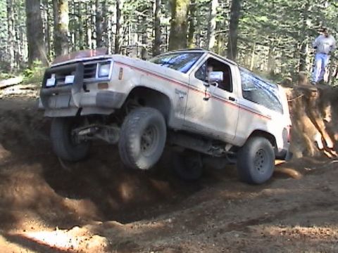 1994 Ford Explorer - A white Ford Bronco II navigates a challenging off-road trail, with one wheel lifted high.