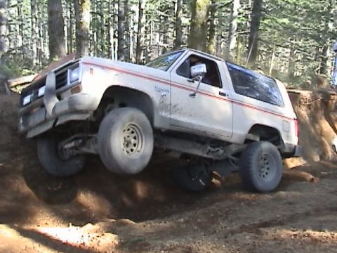 1994 Ford Explorer - A white Ford Bronco II navigates a steep dirt incline in a wooded area.