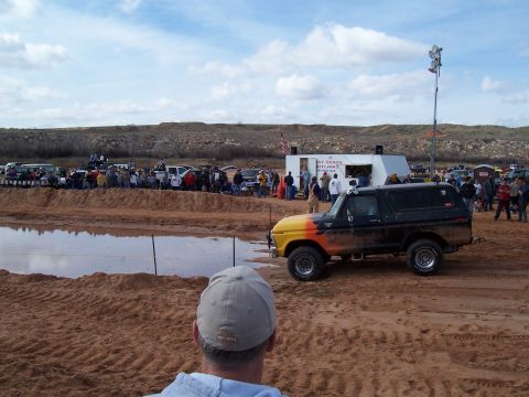 2004 Aston Martin Virage - Off-road event with a modified Ford Bronco in the foreground and spectators in the background.