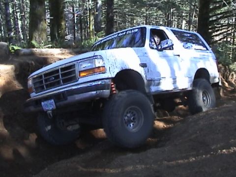 1994 Ford Explorer - A white Ford Bronco navigates a challenging off-road trail in a wooded area.