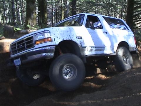 1994 Ford Explorer - White SUV with large tires navigates a dirt trail in a wooded area.